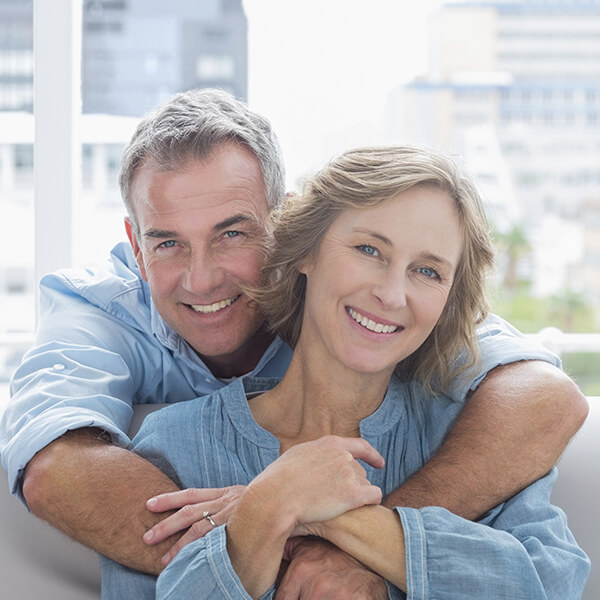 An adult couple hugging while sitting on sofa and smiling