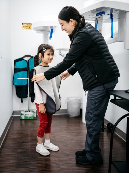 An assistant helps a small patient put on protection before an X-ray.